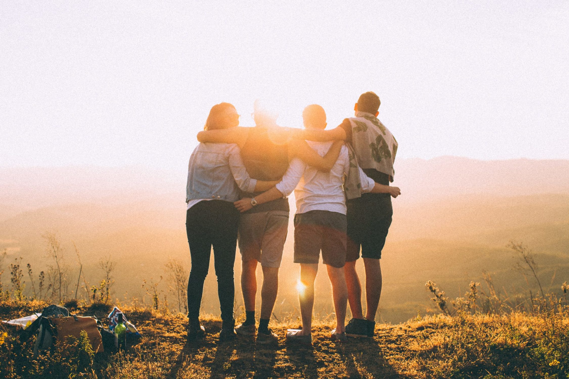 A group of young people, hugging and looking at a sunset.
